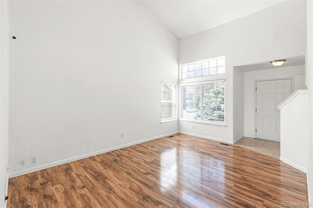 unfurnished room featuring high vaulted ceiling, wood finished floors, and baseboards