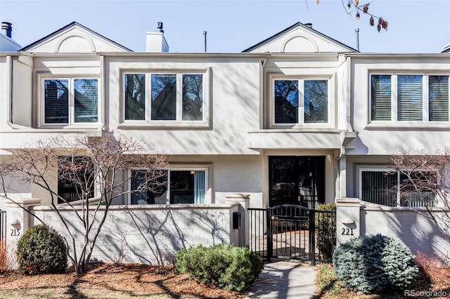 multi unit property featuring a fenced front yard, stucco siding, a chimney, and a gate