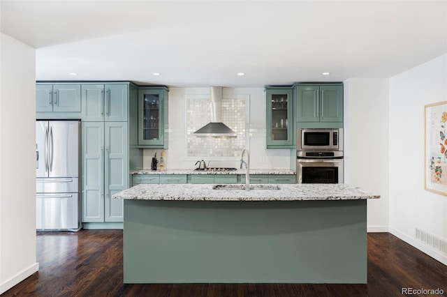 kitchen featuring visible vents, a center island with sink, stainless steel appliances, wall chimney exhaust hood, and a sink