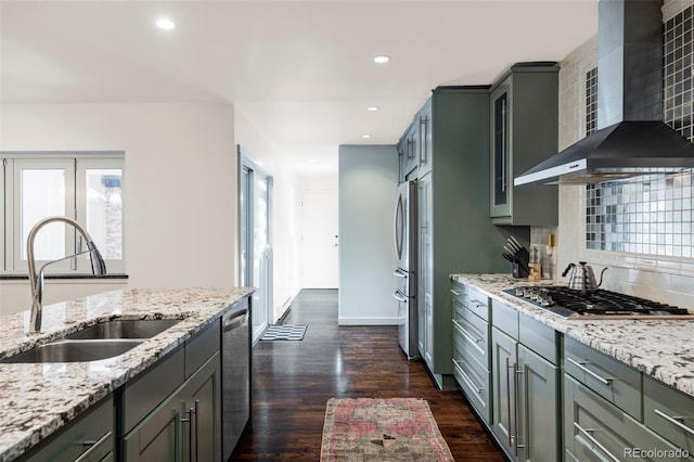 kitchen with dark wood finished floors, stainless steel appliances, a sink, wall chimney exhaust hood, and backsplash