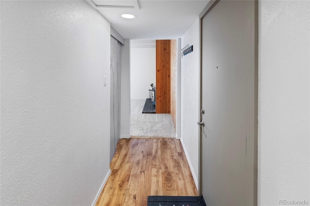 corridor with light wood-style flooring, baseboards, and a textured wall