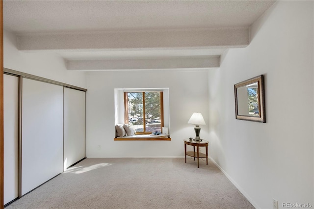 unfurnished bedroom featuring beamed ceiling, carpet, a closet, and a textured ceiling