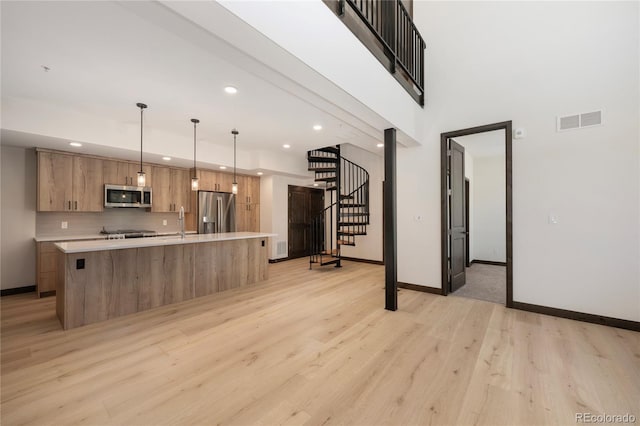 kitchen with a kitchen island with sink, stainless steel appliances, tasteful backsplash, decorative light fixtures, and light wood-type flooring