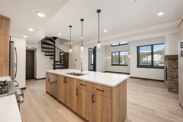 kitchen featuring sink, hanging light fixtures, light hardwood / wood-style flooring, an island with sink, and stainless steel appliances