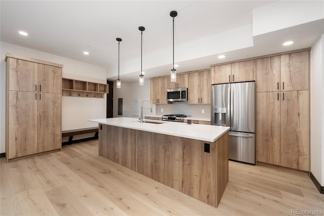 kitchen with pendant lighting, sink, light hardwood / wood-style flooring, stainless steel appliances, and an island with sink