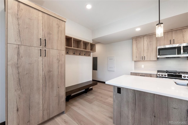 kitchen with pendant lighting, backsplash, electric panel, stainless steel appliances, and light wood-type flooring