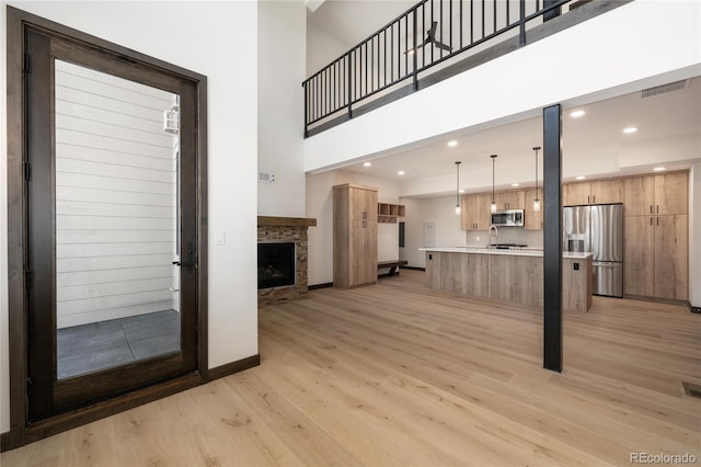 unfurnished living room with sink, a stone fireplace, light hardwood / wood-style floors, and a high ceiling