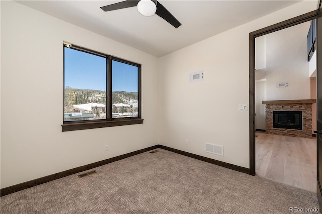 spare room with a stone fireplace, ceiling fan, and carpet flooring