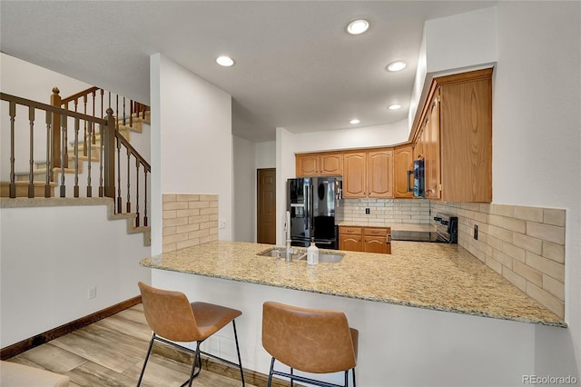 2972 W Long Dr Unit C, Littleton, CO 80120 - kitchen featuring black fridge, stove, backsplash, light wood-style floors, and a peninsula