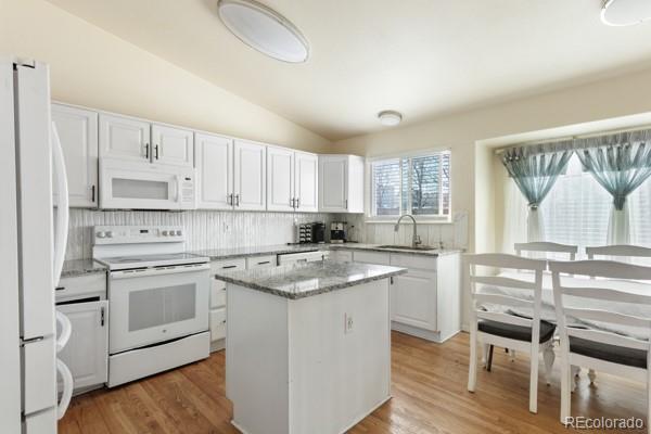 kitchen with sink, white cabinetry, light stone counters, a kitchen island, and white appliances