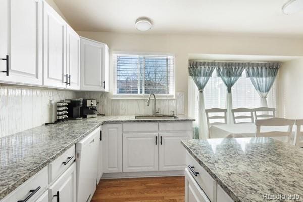 kitchen with sink, dishwasher, light stone counters, wood-type flooring, and white cabinets