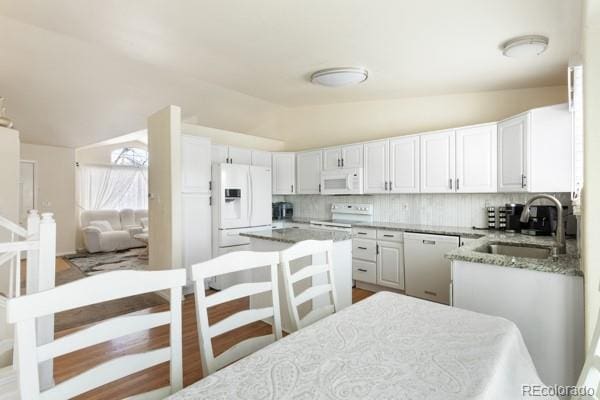 kitchen with vaulted ceiling, sink, white cabinets, light stone countertops, and white appliances