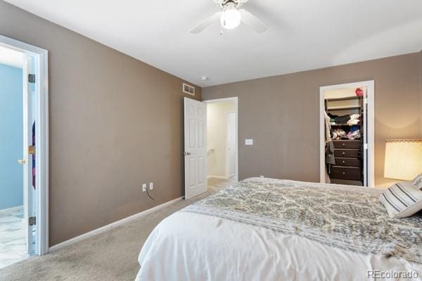 bedroom with a walk in closet, ceiling fan, light carpet, ensuite bath, and a closet