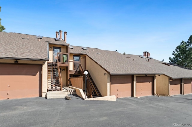 view of property with stucco siding, roof with shingles, and stairs