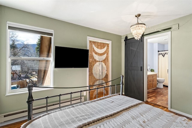 bedroom with wood finished floors, ensuite bathroom, a barn door, and a baseboard radiator