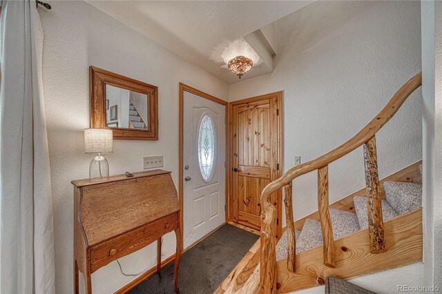 entrance foyer with stairs, a textured wall, and carpet floors