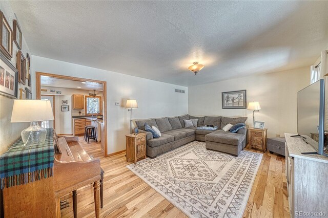 living room with visible vents, light wood-style flooring, and a textured ceiling