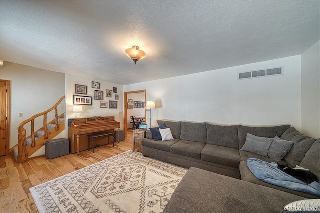 living area featuring stairs, light wood-style floors, visible vents, and a textured ceiling