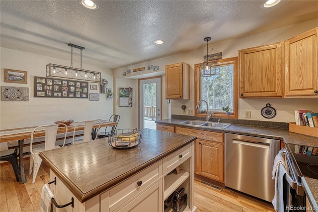 kitchen with light wood-style flooring, a sink, appliances with stainless steel finishes, pendant lighting, and dark countertops