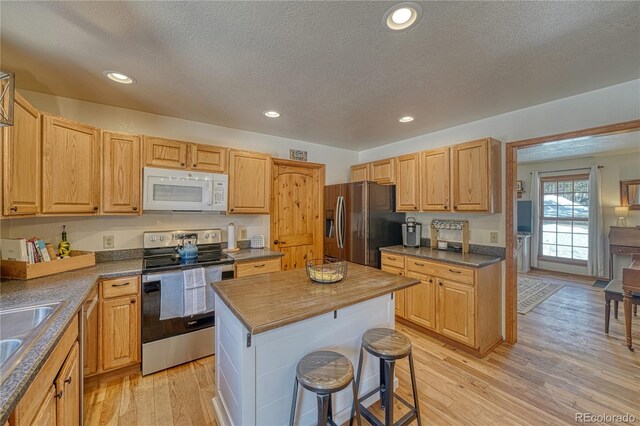 kitchen with a kitchen island, a breakfast bar area, recessed lighting, appliances with stainless steel finishes, and light wood-style floors