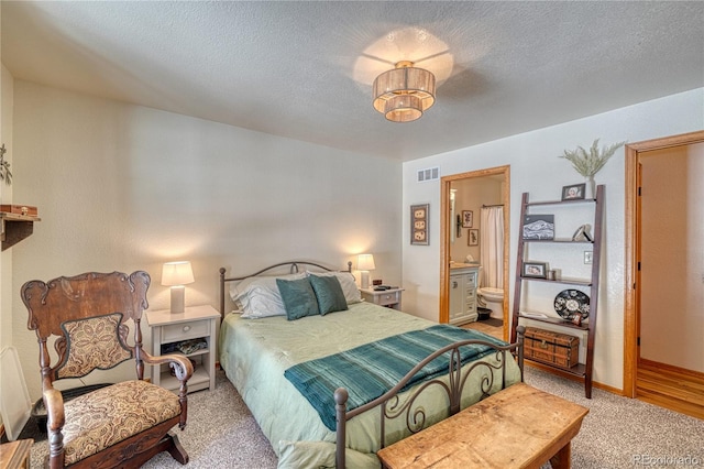 carpeted bedroom with visible vents, baseboards, a textured ceiling, and ensuite bath