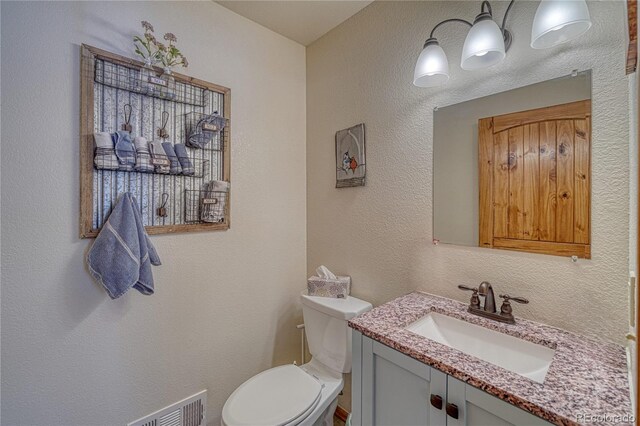 bathroom featuring toilet, vanity, and a textured wall