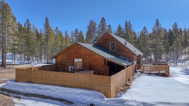 snow covered house featuring fence and a wooden deck