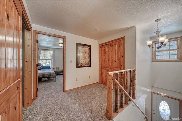 corridor with carpet, an upstairs landing, baseboards, and a textured ceiling