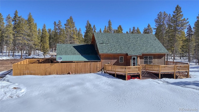 snow covered back of property with a wooden deck and a shingled roof