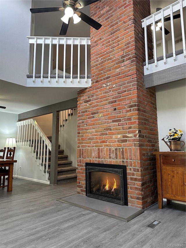 unfurnished living room with ceiling fan, hardwood / wood-style flooring, a towering ceiling, and a brick fireplace