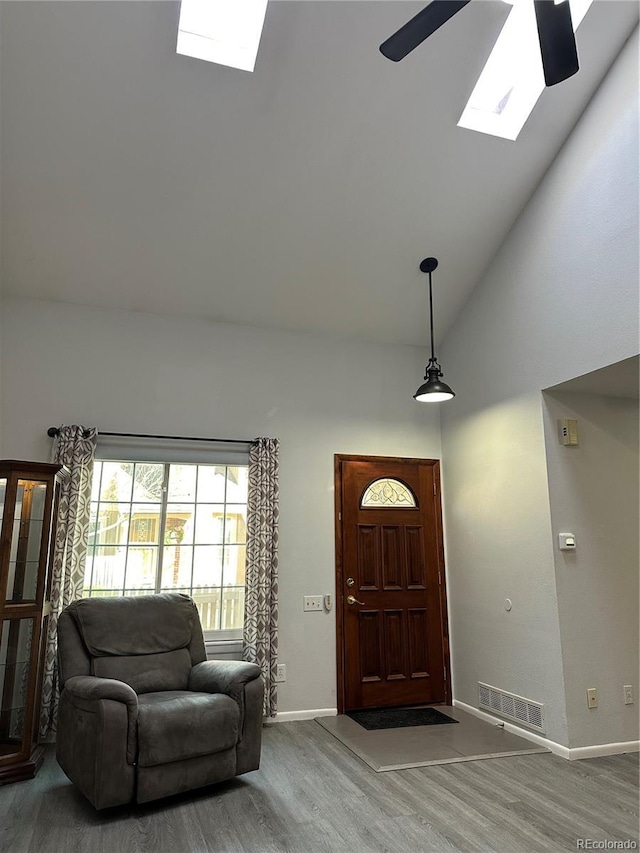 entrance foyer featuring hardwood / wood-style flooring, ceiling fan, high vaulted ceiling, and a skylight