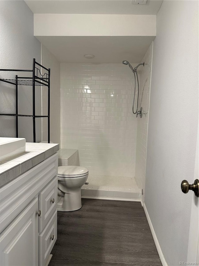 bathroom with wood-type flooring, toilet, vanity, and a tile shower