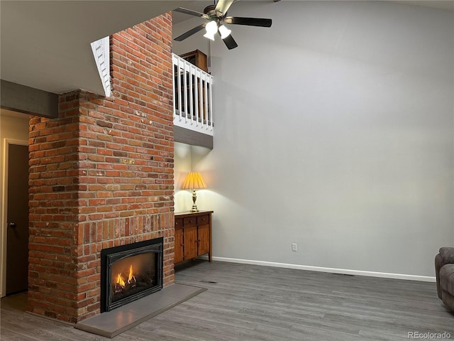 unfurnished living room featuring hardwood / wood-style flooring, a towering ceiling, ceiling fan, and a brick fireplace