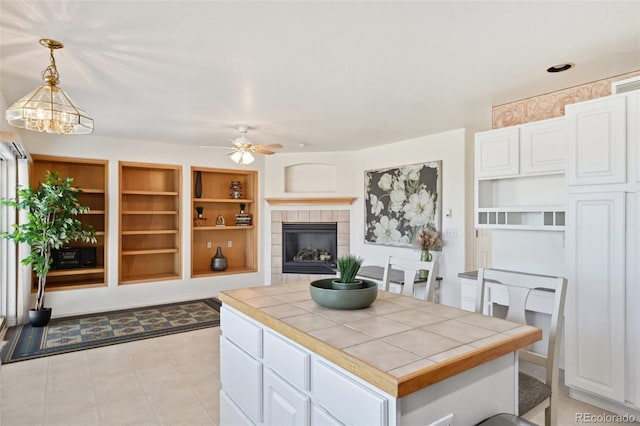 16275 Electra St, Brighton, CO 80603 - kitchen featuring a ceiling fan, hanging light fixtures, a fireplace, white cabinets, and tile counters