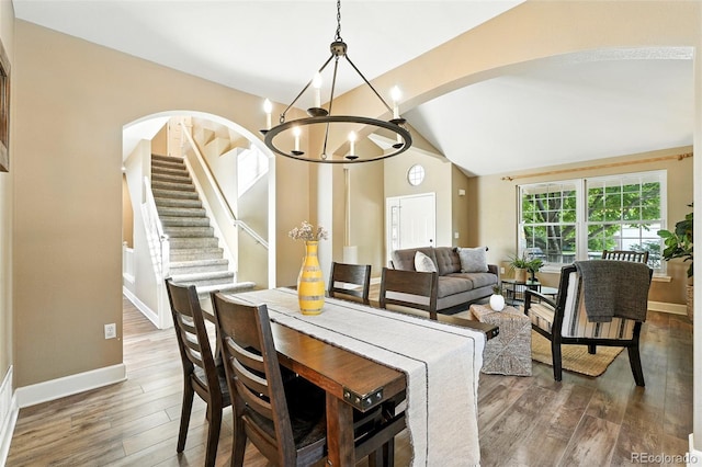 4253 Lark Sparrow St, Highlands Ranch, CO 80126 - dining space featuring arched walkways, wood finished floors, vaulted ceiling, a chandelier, and stairway