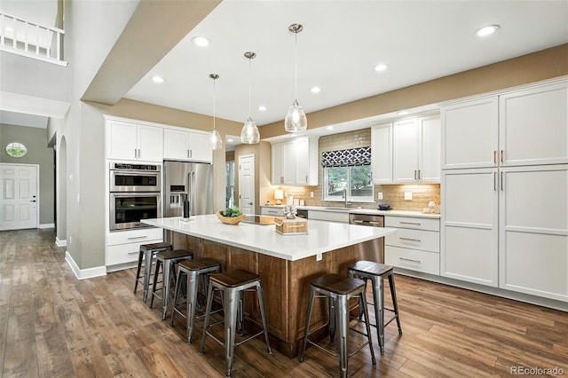 4253 Lark Sparrow St, Highlands Ranch, CO 80126 - kitchen with appliances with stainless steel finishes, a breakfast bar area, dark wood-type flooring, white cabinetry, and recessed lighting