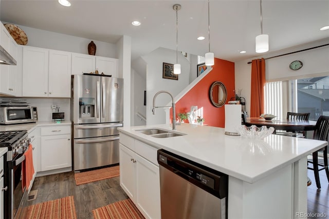 kitchen with dark wood-style floors, an island with sink, a sink, white cabinets, and appliances with stainless steel finishes