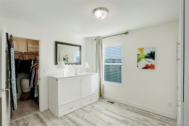 bedroom featuring a spacious closet, visible vents, baseboards, light wood-style floors, and a closet