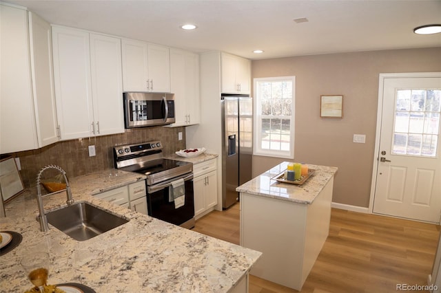 kitchen with appliances with stainless steel finishes, sink, white cabinets, light stone counters, and a healthy amount of sunlight