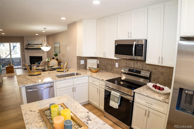 kitchen with pendant lighting, sink, a large fireplace, stainless steel appliances, and light stone countertops