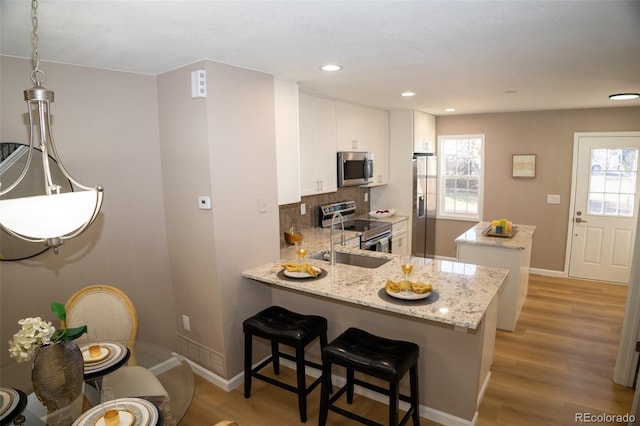 kitchen with stainless steel appliances, light hardwood / wood-style floors, light stone countertops, white cabinets, and kitchen peninsula