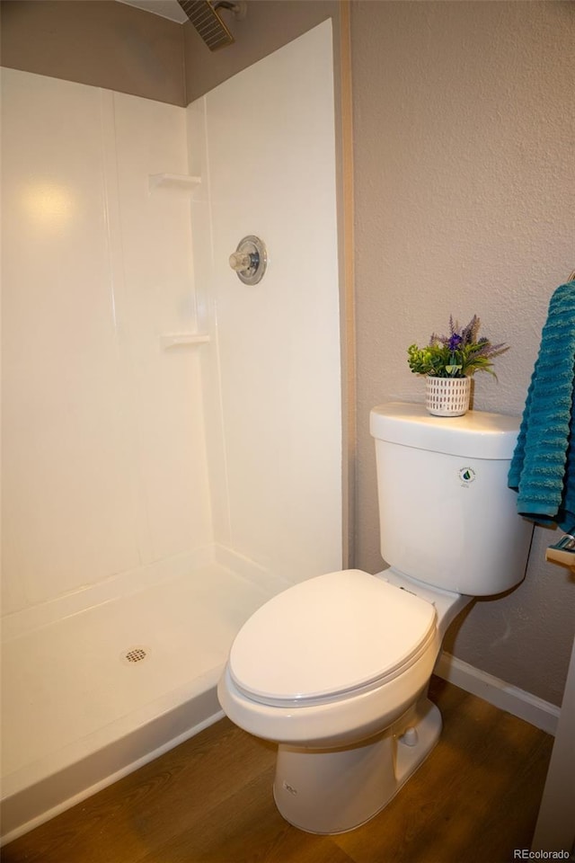 bathroom with hardwood / wood-style flooring, a shower, and toilet