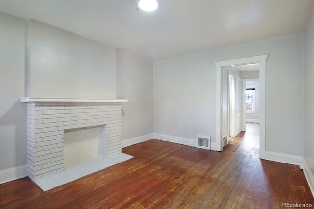 unfurnished living room featuring dark hardwood / wood-style flooring and a brick fireplace