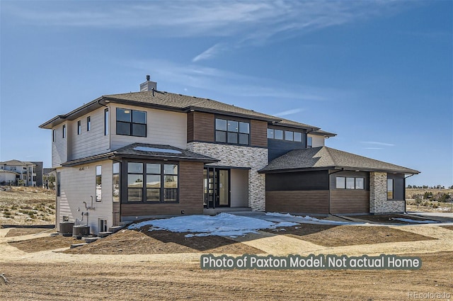 prairie-style home with stone siding, cooling unit, and a chimney