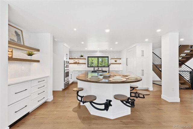 kitchen featuring a breakfast bar, a kitchen island, double oven, light hardwood / wood-style flooring, and white cabinetry