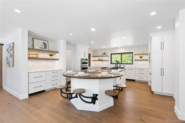 kitchen featuring a kitchen bar, stainless steel double oven, white cabinets, light hardwood / wood-style floors, and a kitchen island