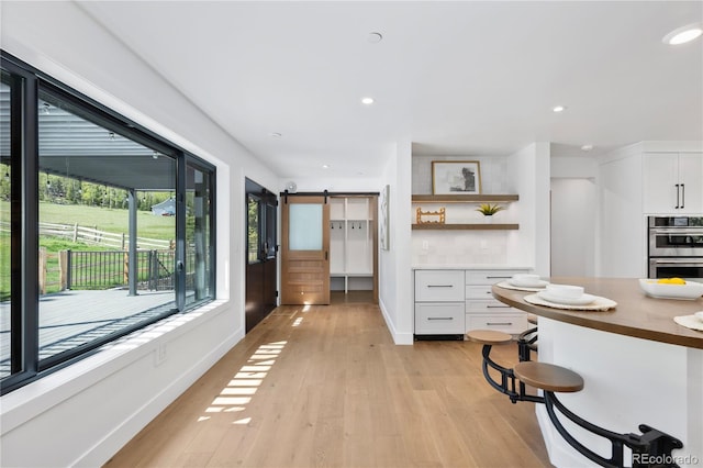 kitchen with double oven, a barn door, white cabinetry, and light wood-type flooring