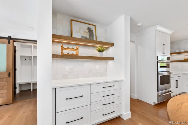 kitchen with a barn door, white cabinetry, double oven, and backsplash