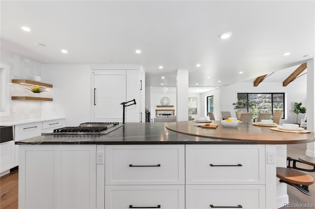 kitchen with stainless steel gas stovetop, a kitchen island, white cabinetry, and dark stone counters