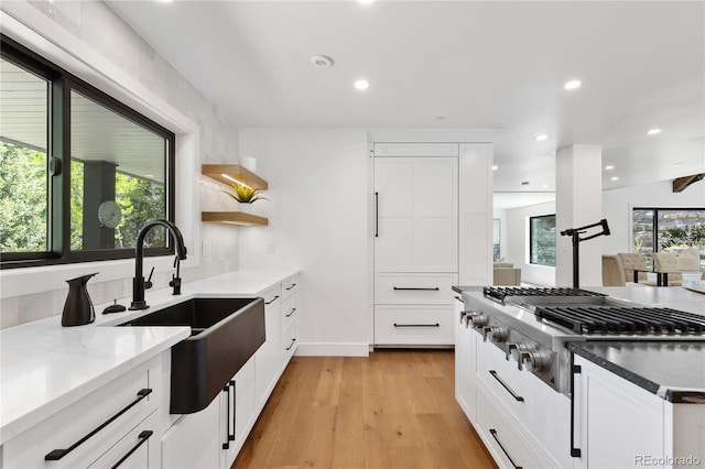 kitchen featuring dark stone counters, white cabinets, sink, light hardwood / wood-style floors, and stainless steel gas cooktop